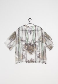 Blouse légère à manches courtes avec un motif floral gris et vert, dotée d'un col rond et d'un dos ouvert. Accrochée à un crochet noir.