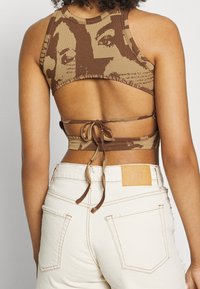 Top corto de punto marrón con un diseño texturizado y cierre atado en la espalda. Combinado con pantalones blancos de talle alto que exhiben una etiqueta de cuero.