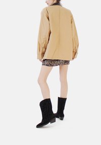 Jachetă supradimensionată bej, fustă mini cu imprimeu leopard și cizme negre din suede până la genunchi cu toc mic. Material neted, design ajustat.