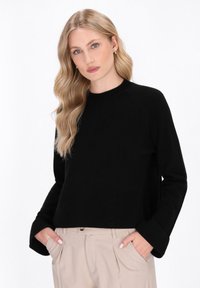 Sort strikket sweater med rund hals og lange ærmer, der har en afslappet pasform og ribbede mansjetter. Kombineret med lyse beige bukser.