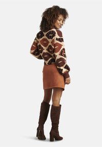 Knit sweater with a geometric pattern in brown, cream, and rust; paired with a rust-colored suede mini skirt and brown knee-high heeled boots.