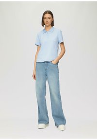 Lichtblauw polo shirt met knoopkraag, gecombineerd met losse lichtdenim jeans en witte platform sneakers.