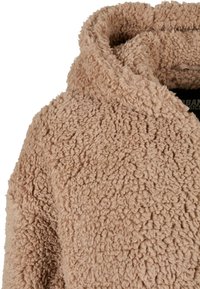Tan, fuzzy fleecejakke med høj krave og blød tekstur. Stoffet har et luksuriøst, shaggy udseende uden synligt hardware.