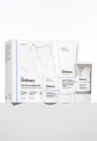Zestaw The Ordinary do twarzy i ciała zawiera trzy butelki kremu: białą emulsję do ciała, białe mleczko do ciała oraz szary tubę, wszystkie o minimalistycznym designie.