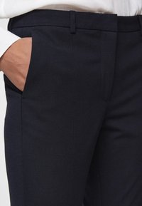 Granatowe spodnie garniturowe o gładkiej teksturze, slim fit, z bocznymi kieszeniami i eleganckim pasem, z subtelnym wzorem materiału.