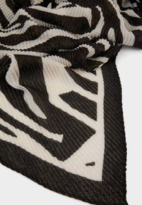 Sciarpa a strisce in bianco e nero con texture a coste e riflessi metallici, caratterizzata da una forma triangolare e strisce stilizzate audaci.