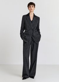 Completo su misura a quadri grigio scuro con giacca doppiopetto, rever neri e pantaloni a gamba larga. Scarpe lucide nere a punta.