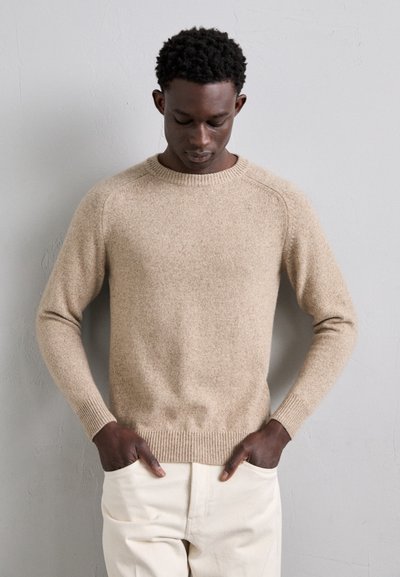 Beige kötött pulóver bordás kerek nyakkal, hosszú ujjakkal és feszes aljjal. Puha tapintású, enyhén foltos felülettel.