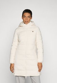 Lange, lichtromige pufferjas met capuchon, ritssluiting en doorgestikte ontwerp. Heeft elastische manchetten en een klein logo op de borst.