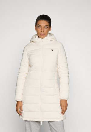 Manteau matelassé long, couleur crème pâle, avec capuche, fermeture éclair et design matelassé. Équipé de poignets élastiques et d'un petit logo sur la poitrine.