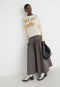 Kremasta sv sweater z napisom "LET IT SNOW" v zlati špici, v kombinaciji s temnosivo maxi krilo in sijočimi srebrnimi platform čevlji. Vključena črna torbica.
