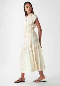 Krémové šaty s černými puntíky, krátké rukávy, zapínací límec, stažený pas a vícevrstvá sukni. V kombinaci s černými sandály.