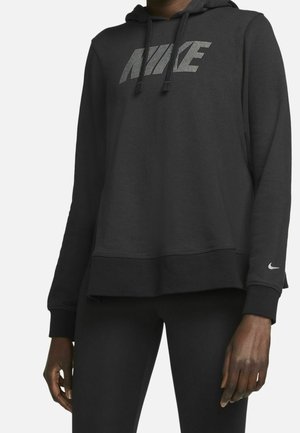 Persona con sudadera negra de Nike con logotipo de puntos en el pecho y pequeño símbolo Swoosh en la manga, combinada con pantalones negros.