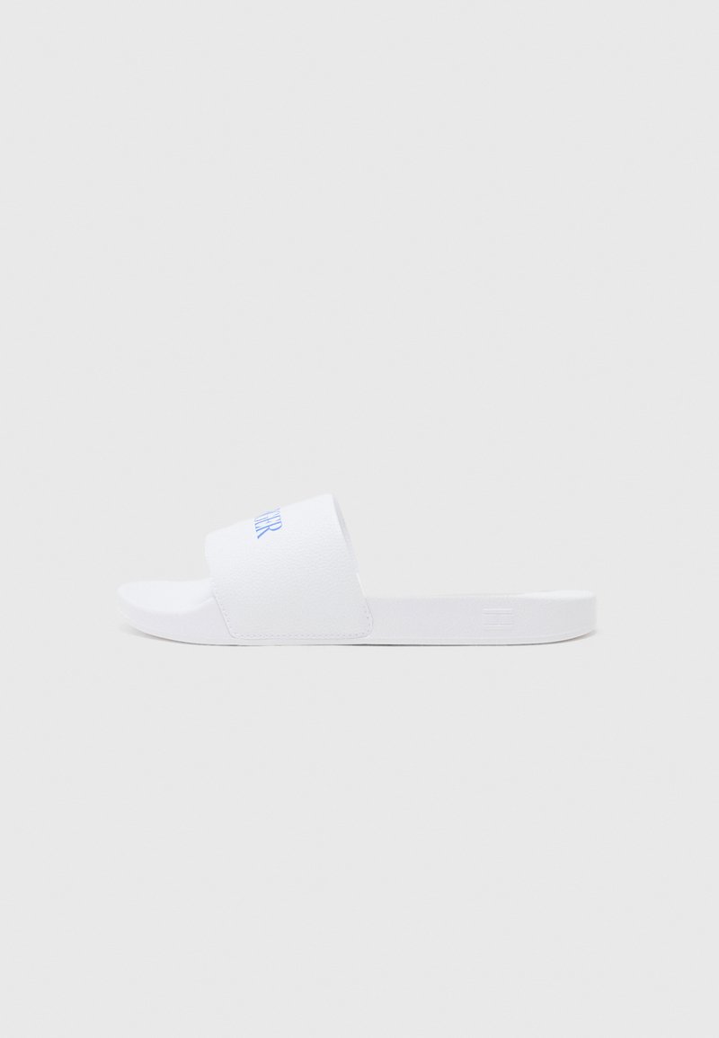 White slide sandals feature a textured strap with blue branding. Flat sole design with a minimalist shape and smooth finish.