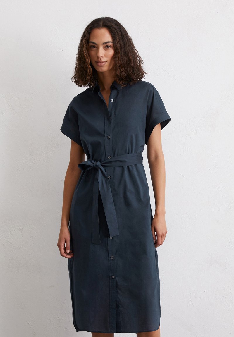 Abito camicia in lino blu scuro con maniche corte, chiusura con bottoni sul davanti e cintura da annodare in vita; presenta un taglio diritto lungo fino alla caviglia.