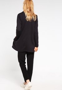 Černé dlouhé rukávy top s volnou siluetou, kombinované s úzkými černými kalhotami. Oba kusy mají hladkou texturu a jednoduchý design.