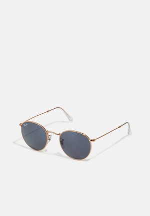 Occhiali da sole ovali con lenti scure, montatura in metallo dorato e punte delle tempie in plastica trasparente. Presentano bracci sottili e un design minimalista.