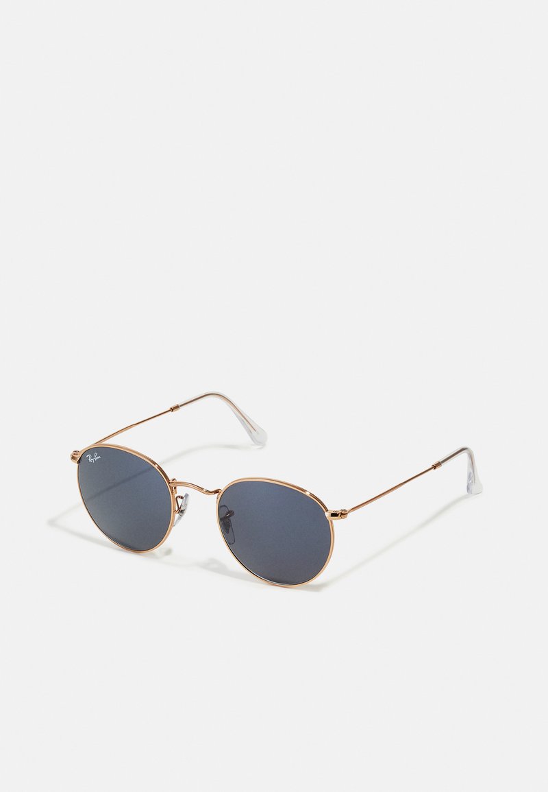 Occhiali da sole ovali con lenti scure, montatura in metallo dorato e punte delle tempie in plastica trasparente. Presentano bracci sottili e un design minimalista.