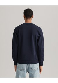 Marinblå sweatshirt med ribbat rundhals, långa ärmar och en figurnära nederkant. Texturerad tyg, bärs med ljusblå denimjeans.