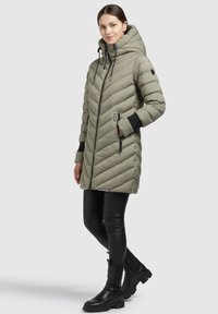 Lättvikts, olivgrön puffjacka med diagonala sömmar, hög krage, justerbar dragsko på huvan och zippered sidofickor.
