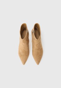 Beige velúr bokacsizma hegyes orral és oldalsó fém cipzárral. Simaságával és elegáns, letisztult formájával tűnik ki.