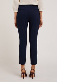 Maritieme op maat gemaakte broeken met een slim fit, twee achterzakken en een gladde textuur, gecombineerd met bordeauxrode hoge hakken.