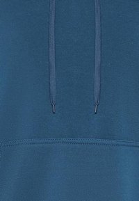 Felpa con cappuccio blu navy dal tessuto morbido, dotata di cordini regolabili e tasca a marsupio. Dettagli di cucitura minimal.