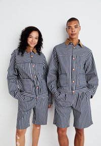Gestreepte set van een jasje en shorts in marineblauw en wit, met contrasterende bruine kraag en oranje knopen, voorzien van zakken en een ontspannen pasvorm.