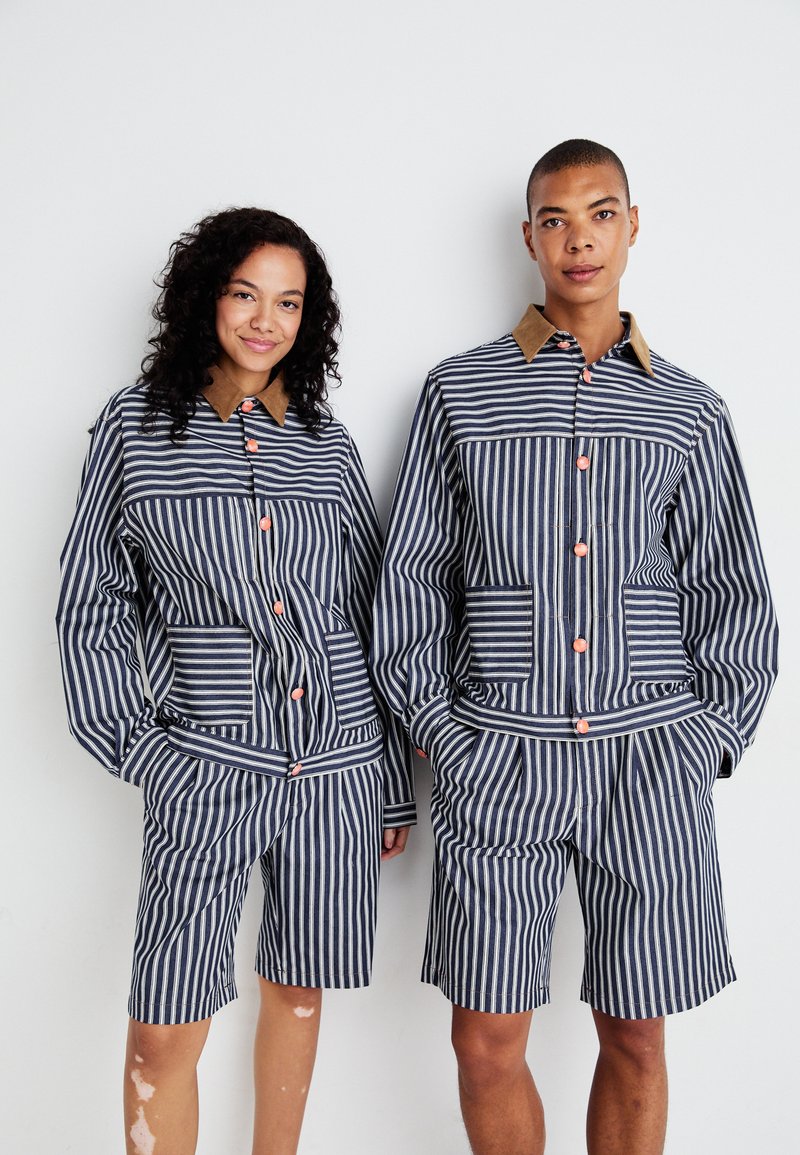 Gestreepte set van een jasje en shorts in marineblauw en wit, met contrasterende bruine kraag en oranje knopen, voorzien van zakken en een ontspannen pasvorm.