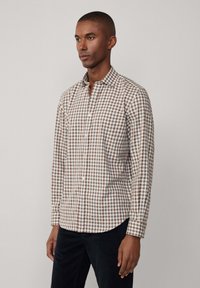 Camicia a maniche lunghe a scacchi marrone e bianca con colletto, chiusura a bottoni e orlo curvo. Realizzata in un tessuto leggero.