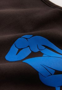 Figura humana abstracta azul tumbada sobre tela marrón oscura con textura y pliegues visibles.