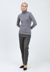 Pull à col roulé gris en matière douce, design ajusté, associé à un pantalon gris foncé et des chaussures à bout pointu noires.