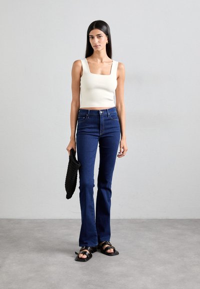 White square-neck crop top, dark blue flared jeans, black woven clutch, black strappy sandals. Smooth fabric, tailored fit, and simple design.