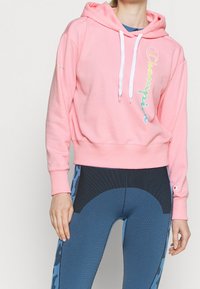 Rosa bomullshoodie med dragsnören och "Champion"-logotyp i graderade färger; kombinerad med blå texturerade leggings med djurtryck.