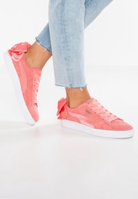 Baskets en daim rose avec des accents en dentelle satinée et un nœud au talon. Présente une tige texturée et une semelle en caoutchouc blanche.