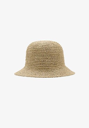 Chapeau seau en paille tissée beige avec bord incliné vers le bas et motif texturé sur fond blanc.