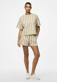 Haut en coton beige rayé et shorts assortis. Le haut a des manches courtes et une coupe décontractée ; les shorts présentent une taille élastique. Chaussures décontractées.