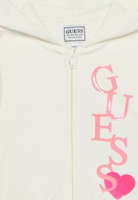 Κρεμ φούτερ με φερμουάρ. Διαθέτει μεγάλα, γυαλιστερά ροζ γράμματα στο μπροστινό μέρος. Περιλαμβάνει κουκούλα για επιπλέον στυλ και ζεστασιά.