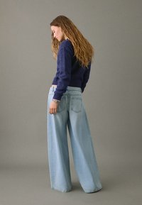 Mornarsko pleteno pulover s skrajšanim dizajnom, v kombinaciji s svetlo modrimi širokimi hlačami. Mehka tekstura, rebrasti manšeti in detajli na zadnjem žepu.