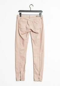 Jeans de mezclilla rosa claro con un corte ajustado, que presentan una textura brillante, cremalleras en los tobillos y dos bolsillos traseros con un detalle de logo en forma de triángulo.