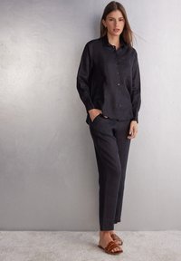 Linnen overhemd en broekenset in donker marineblauw, met knopen, zakdetail en een relaxte pasvorm. Gecombineerd met bruine sandaaltjes met banden.