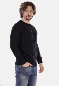 Maglione nero lavorato a maglia con un motivo a diamante testurizzato, scollo rotondo e polsini a costine, abbinato a jeans blu.
