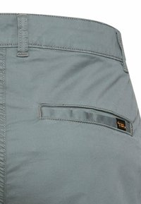 Grau melierte Hosen Tasche mit Einzelnaht und kleinem schwarzen rechteckigen Markenetikett, das nahe der Taschenkante angenäht ist.