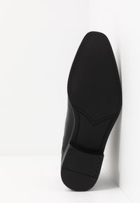 Černá kožená podrážka boty, hladká textura s špičatým tvarem. Obsahuje šité detaily a obdélníkovou základnu podpatku.