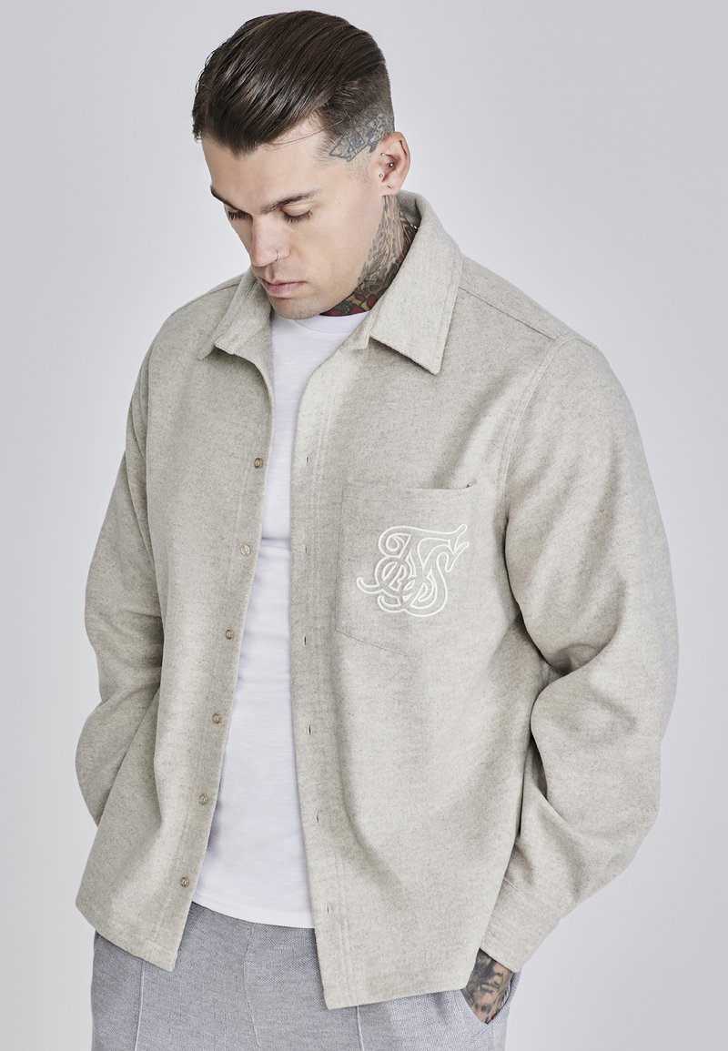 Light gray button-up shirt made of soft fabric, featuring a chest pocket with white embroidered detailing, and a spread collar design.