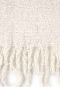 Miękka, kremowa dzianina z luźnymi, puszystymi frędzlami zwisającymi na dolnej krawędzi.