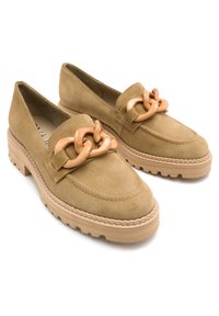 Beżowe zamszowe loafersy z masywną podeszwą i wyraźnym brązowym łańcuchem. Posiadają przeszycia oraz gładką teksturę.