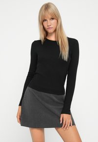Haut noir à manches longues côtelé associé à une mini-jupe à carreaux grise avec des détails drapés, une texture lisse et une coupe ajustée.