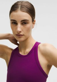 Lila atletisk linne med hög krage och breda ärmhål, tillverkat av ett mjukt tyg, med rena kanter och minimala designdetaljer.