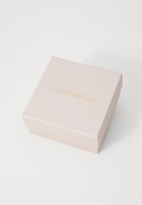 Boîte de marque Coccinelle, de forme carrée, couleur rose doux avec une texture lisse, avec des lettres dorées sur le dessus, couvercle bien structuré.